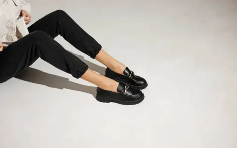 Une tenue décontractée avec un jean noir et une veste claire, rehaussée par une élégante tenue avec mocassin femme orné d'une chaîne dorée.
