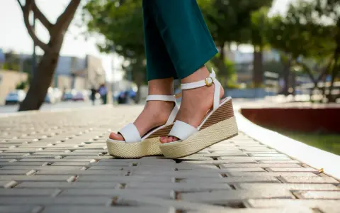Pieds portant des sandales compensées blanches à plateforme sur un trottoir pavé.