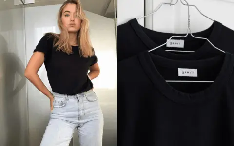 Une jeune femme porte une tenue avec t-shirt noir et jean clair. Deux t-shirts noirs identiques sont accrochés sur des cintres.
