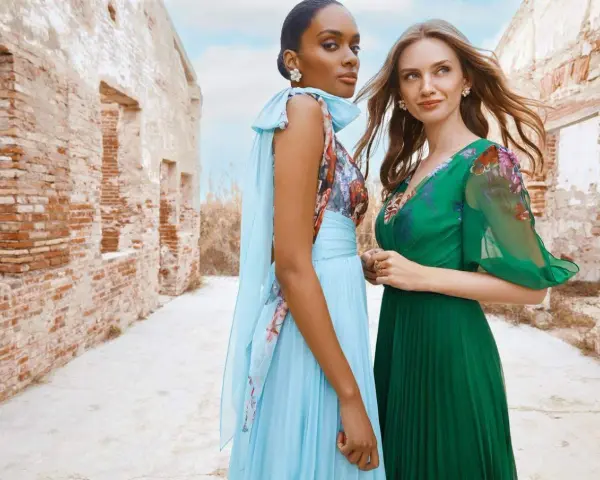 Deux femmes portent des robes élégantes, parfaites pour une tenue mariage avril. L'une est en bleu ciel plissé, l'autre en vert émeraude.