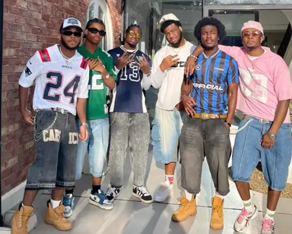 Six hommes posent ensemble, portant des tenues inspirées des années 2000.