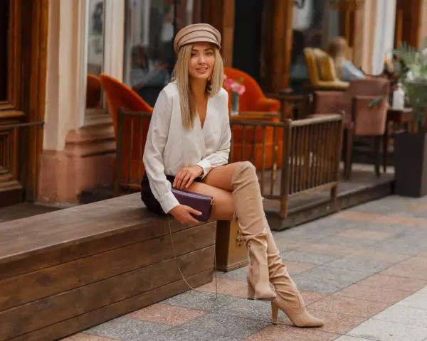 Une femme élégante assise dehors, portant une tenue chic avec des bottes hautes beiges. Idée de comment porter des bottes hautes marrons avec style.