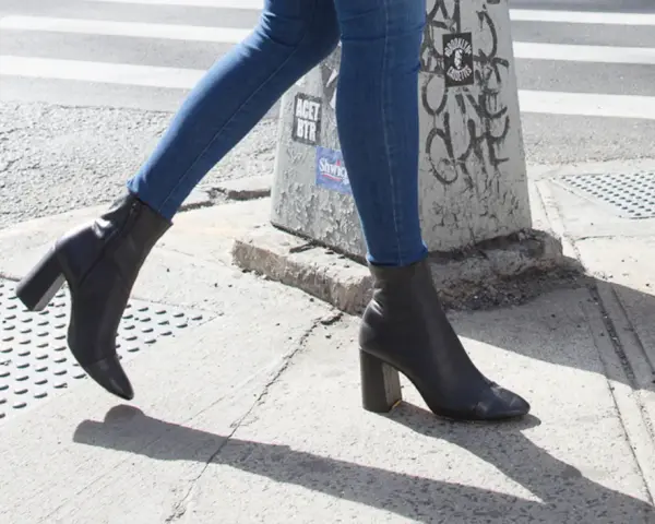 Une femme marche dans la rue avec un jean slim et des bottines noires à talons.