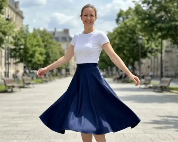 Une femme en talon et jupe évasée bleue danse joyeusement dans une rue parisienne bordée d'arbres.