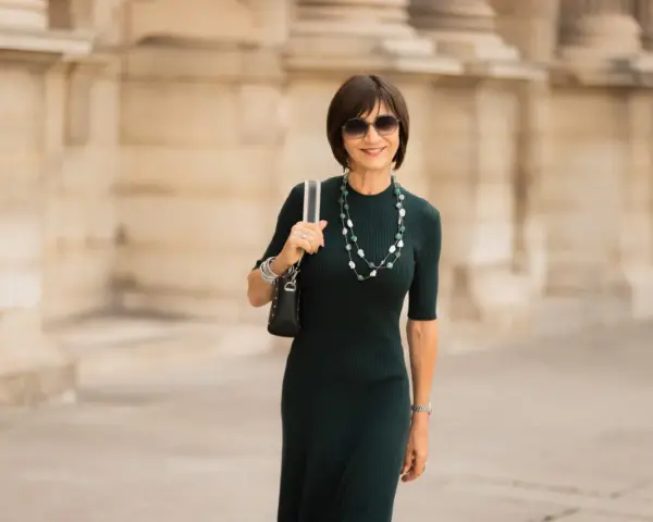 Une femme élégante porte une robe midi vert foncé, un collier de perles et des lunettes de soleil. La robe midi définition est une longueur polyvalente.