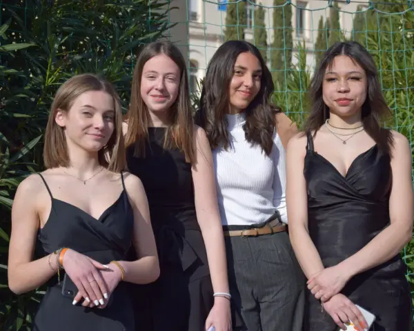 Quatre jeunes femmes posent, habillées élégamment. Idées pour comment s'habiller pour l'Aïd : robes noires, haut blanc chic, et accessoires discrets.
