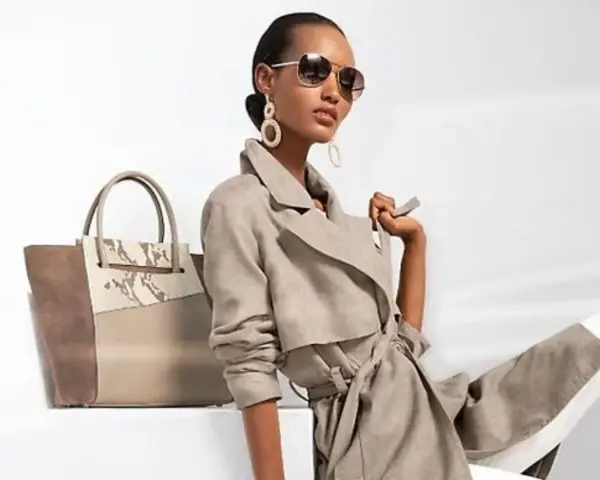 Une femme incarne le **style classique femme** avec un trench léger, des lunettes aviateur et un grand sac bicolore.