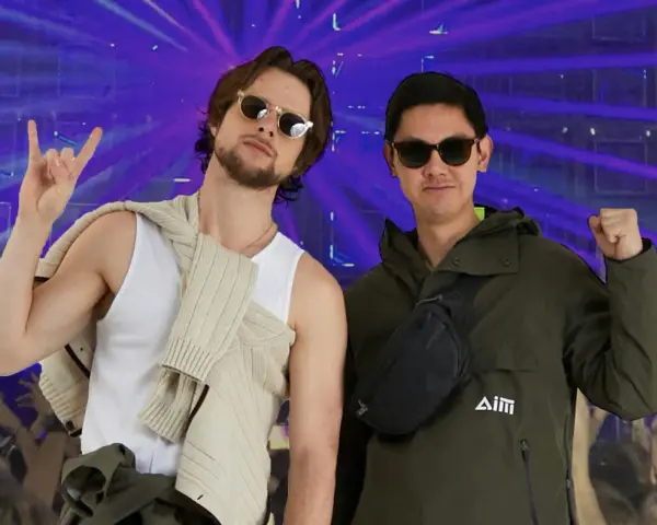 Deux amis profitent d'un concert, l'un fait un signe rock'n'roll, l'autre un poing levé. Leur tenue festival pluie est parfaite pour l'ambiance.