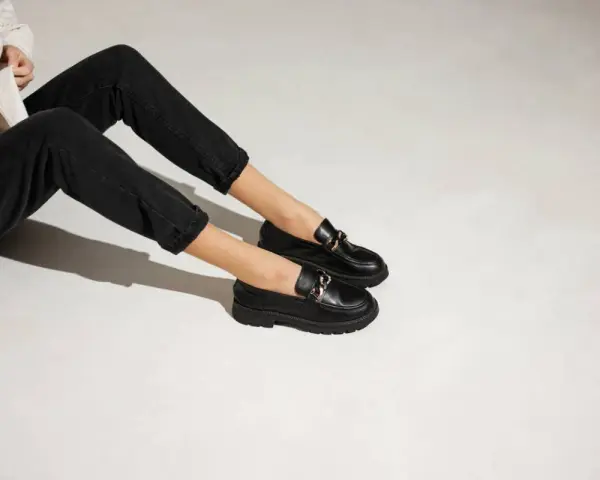 Une tenue décontractée avec un jean noir et une veste claire, rehaussée par une élégante tenue avec mocassin femme orné d'une chaîne dorée.