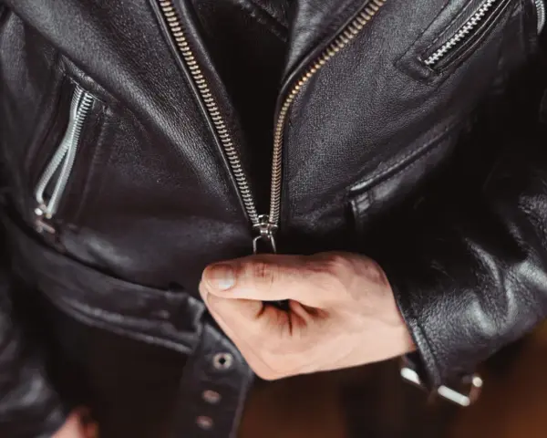 Main d'homme fermant la fermeture éclair d'une veste en cuir noire, partie d'un outfit classique et intemporel.