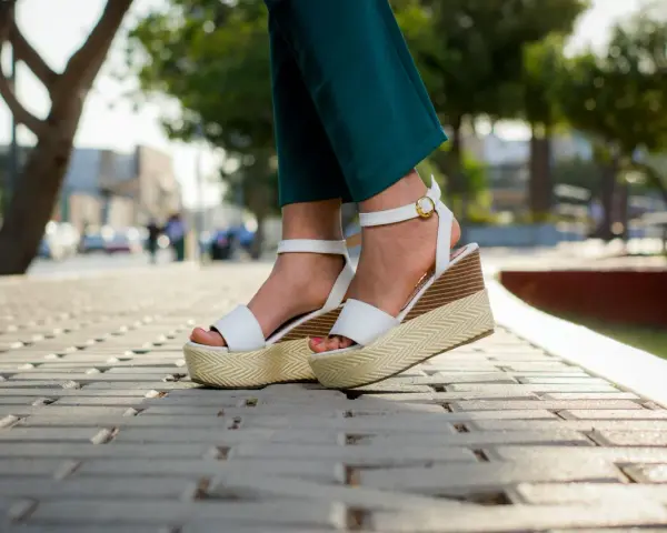 Pieds portant des sandales compensées blanches à plateforme sur un trottoir pavé.