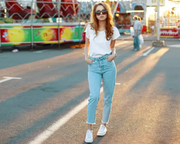 Une jeune femme porte un jean mom et des baskets blanches, un look parfait pour une journée à la fête foraine.