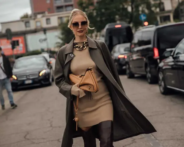 Une femme élégante pose dans la rue, portant une robe courte beige et un long manteau kaki. Elle montre quelle veste porter avec une robe courte pour un look chic.