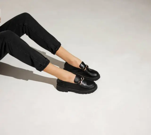 Une tenue décontractée avec un jean noir et une veste claire, rehaussée par une élégante tenue avec mocassin femme orné d'une chaîne dorée.