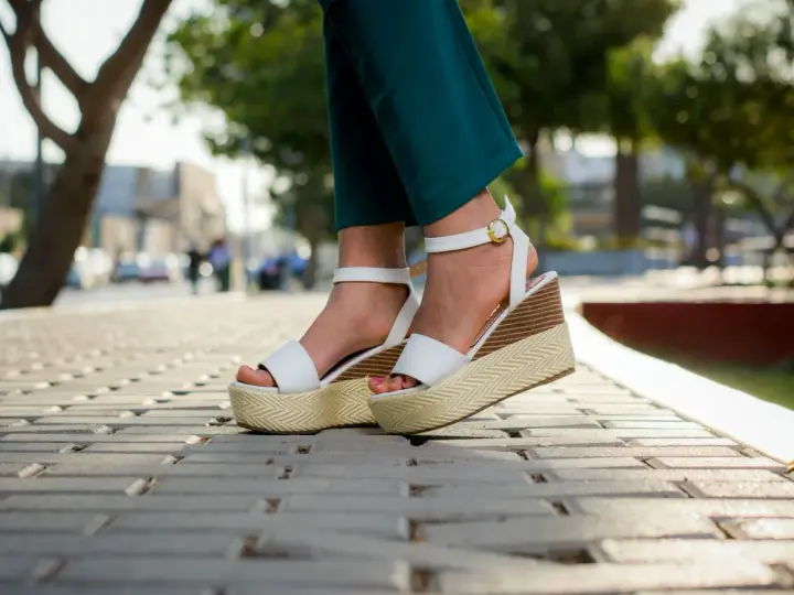 Pieds portant des sandales compensées blanches à plateforme sur un trottoir pavé.