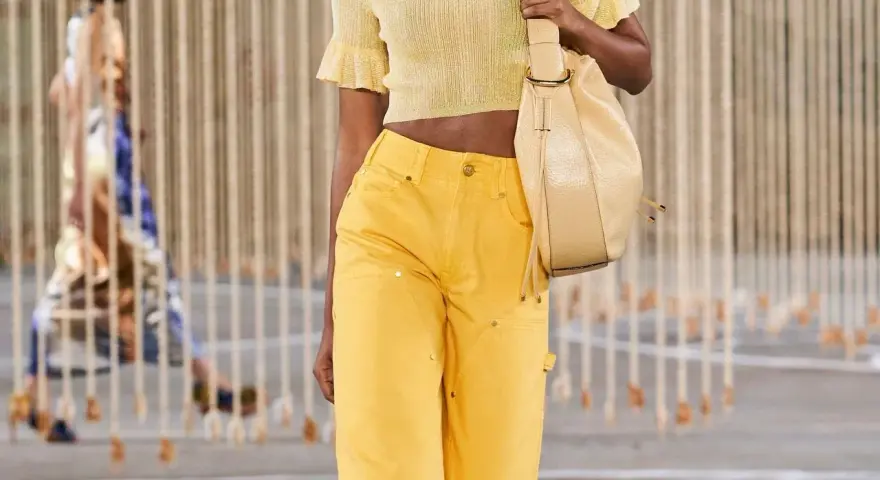 Mannequin portant une tenue de soirée en jean jaune vif, un haut court assorti et un sac beige.