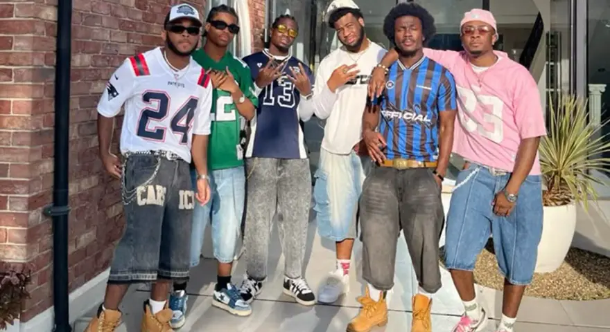 Six hommes posent ensemble, portant des tenues inspirées des années 2000.