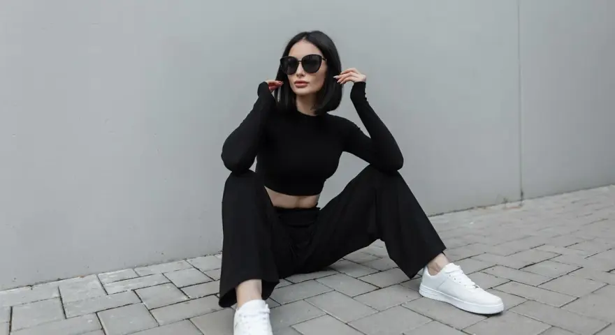 Une femme en tenue noire, crop top et pantalon large, assise sur des pavés. Idée de comment porter un pantalon large avec des baskets blanches.