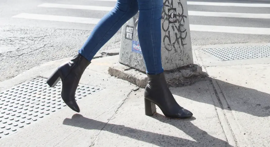 Une femme marche dans la rue avec un jean slim et des bottines noires à talons.