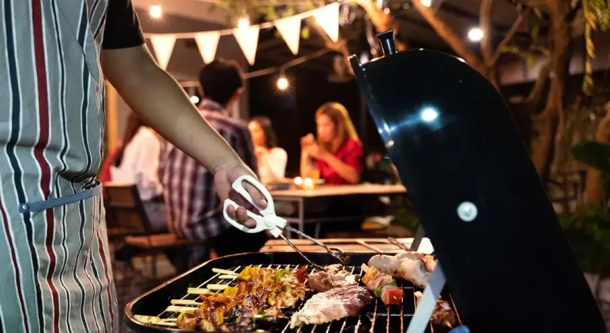 Un homme en tablier rayé prépare un barbecue. Idéal pour savoir comment s'habiller pour un barbecue : décontracté et pratique !
