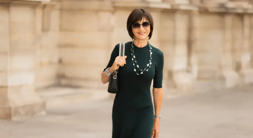 Une femme élégante porte une robe midi vert foncé, un collier de perles et des lunettes de soleil. La robe midi définition est une longueur polyvalente.