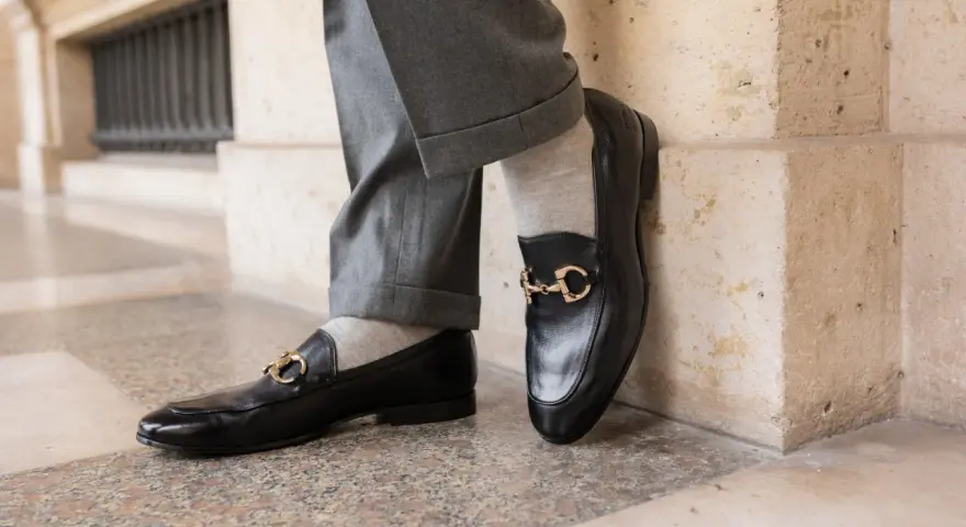 Un homme porte un pantalon gris retroussé et une chaussette mocassin noire avec une boucle dorée.
