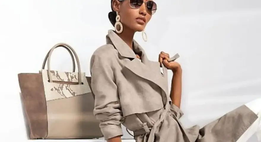 Une femme incarne le **style classique femme** avec un trench léger, des lunettes aviateur et un grand sac bicolore.