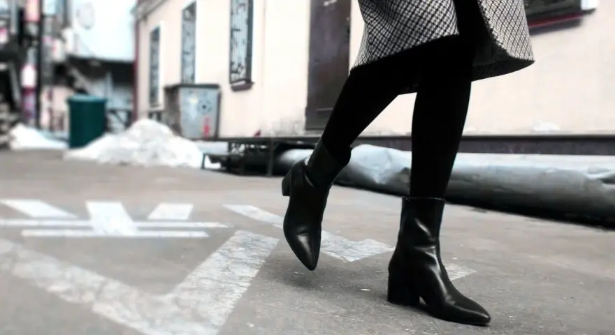 Une femme porte une tenue avec des chelsea boots femme noires, un manteau à carreaux et des collants.