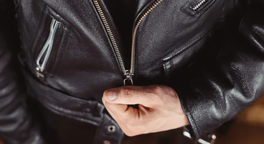 Main d'homme fermant la fermeture éclair d'une veste en cuir noire, partie d'un outfit classique et intemporel.