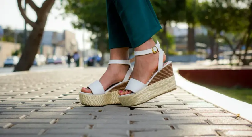 Pieds portant des sandales compensées blanches à plateforme sur un trottoir pavé.