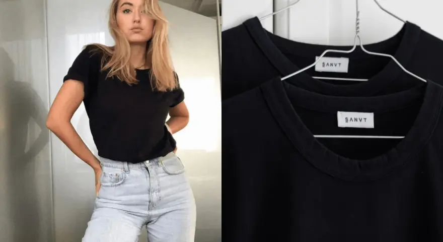Une jeune femme porte une tenue avec t-shirt noir et jean clair. Deux t-shirts noirs identiques sont accrochés sur des cintres.