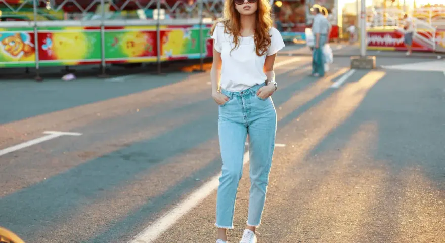 Une jeune femme porte un jean mom et des baskets blanches, un look parfait pour une journée à la fête foraine.