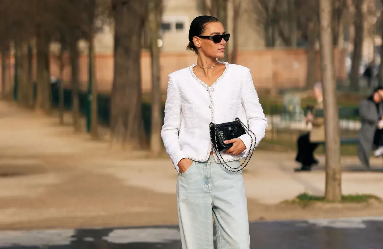 Élégante femme en veste blanche et jean clair, sac noir à chaîne. Un avant-goût du printemps 2026.