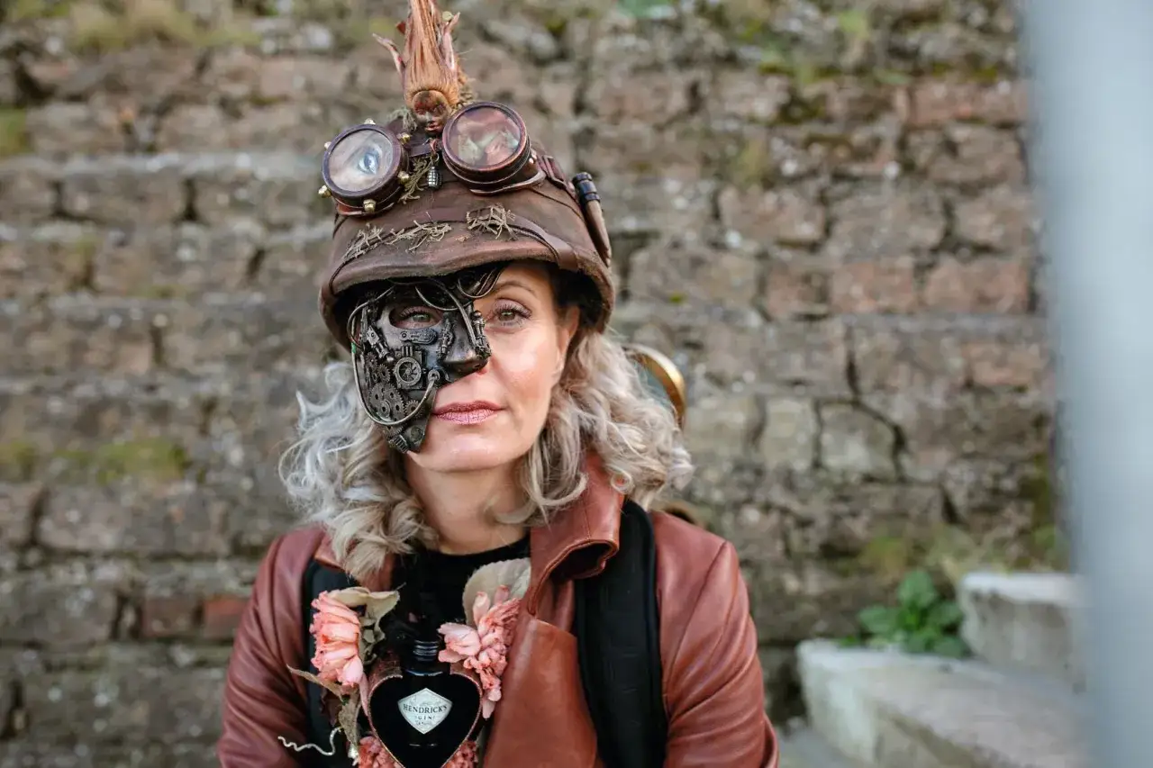 Une femme au style steampunk, portant un masque m&eacute;canique complexe et des lunettes d'aviateur sur un casque orn&eacute;.