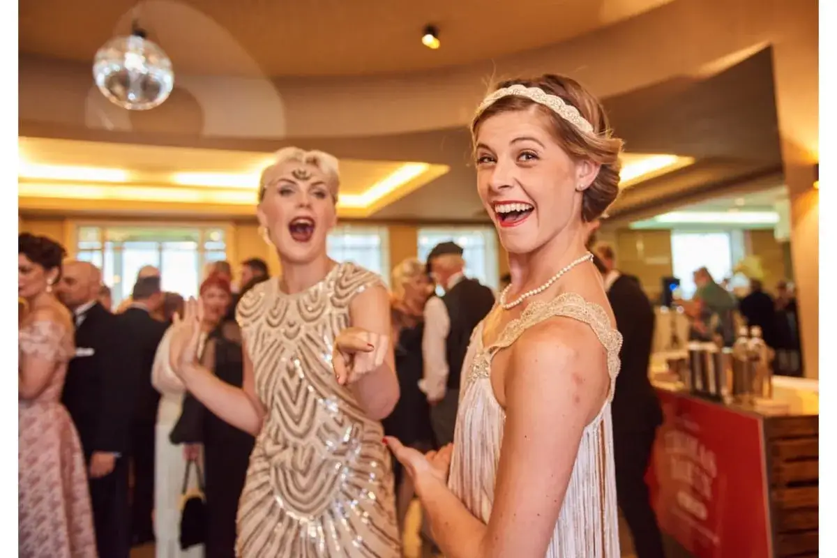 Deux femmes dansent, portant des robes &agrave; paillettes et des bandeaux, une tenue guinguette femme parfaite pour une soir&eacute;e festive.