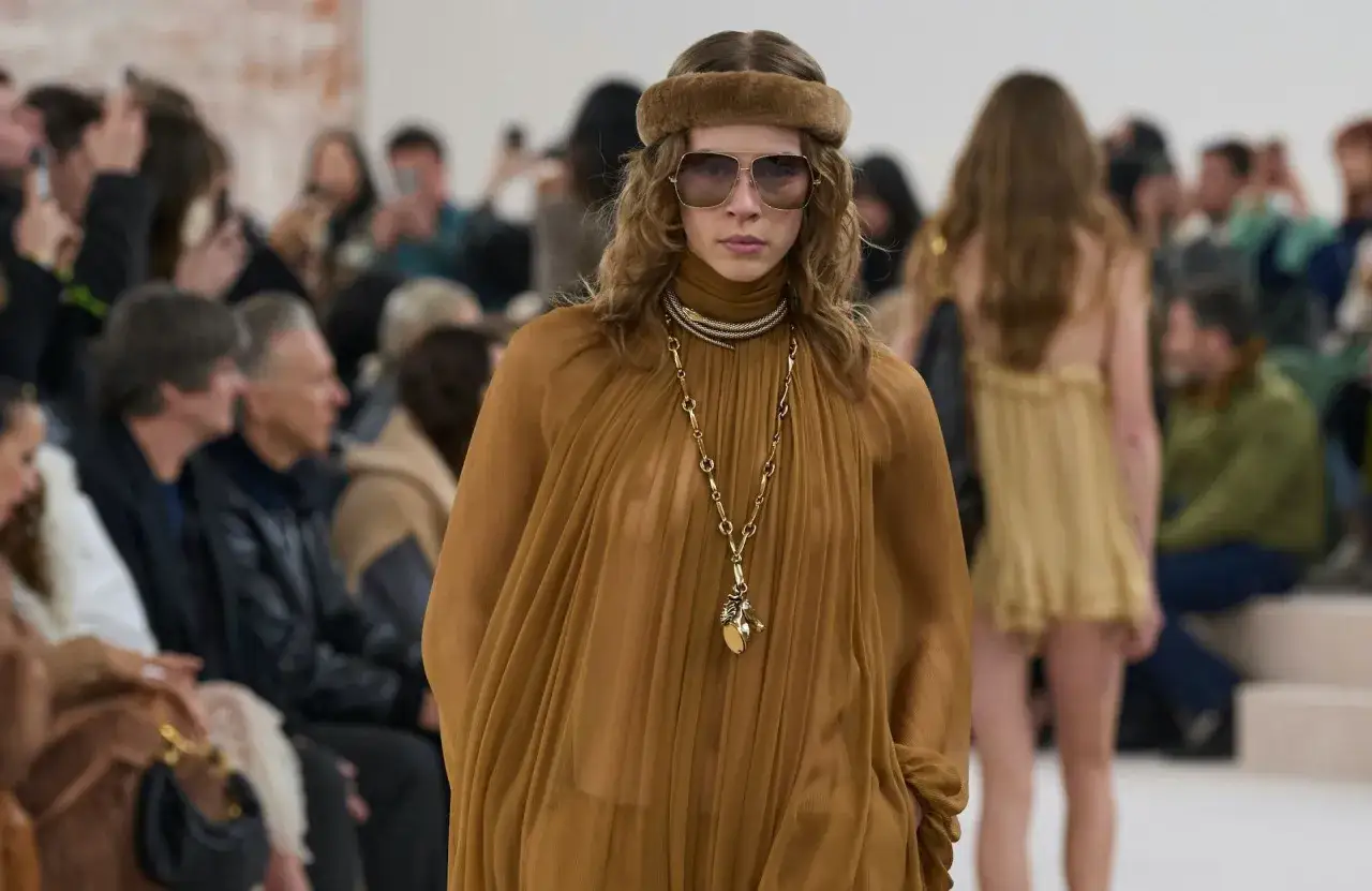 Mannequin au style boh&egrave;me, portant une robe fluide ocre, un bandeau en fausse fourrure et de grandes lunettes de soleil.