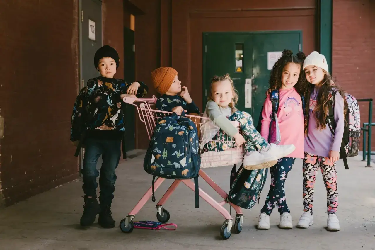 Cinq enfants, pr&ecirc;ts pour la photo de classe, portent des tenues color&eacute;es et des sacs &agrave; dos amusants.