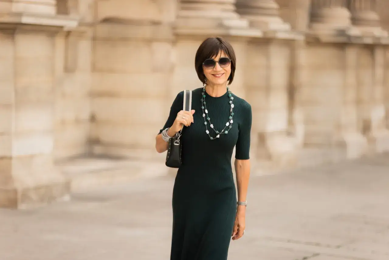 Une femme élégante en robe verte, collier perlé, parfaite pour savoir comment s'habiller pour un vernissage.