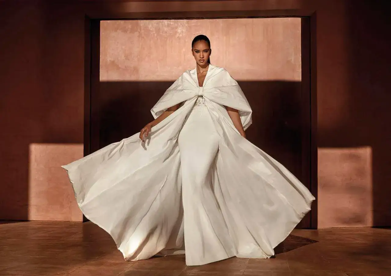 Une femme porte une magnifique tenue de mariage religieux, une robe blanche &eacute;vas&eacute;e avec une cape spectaculaire.