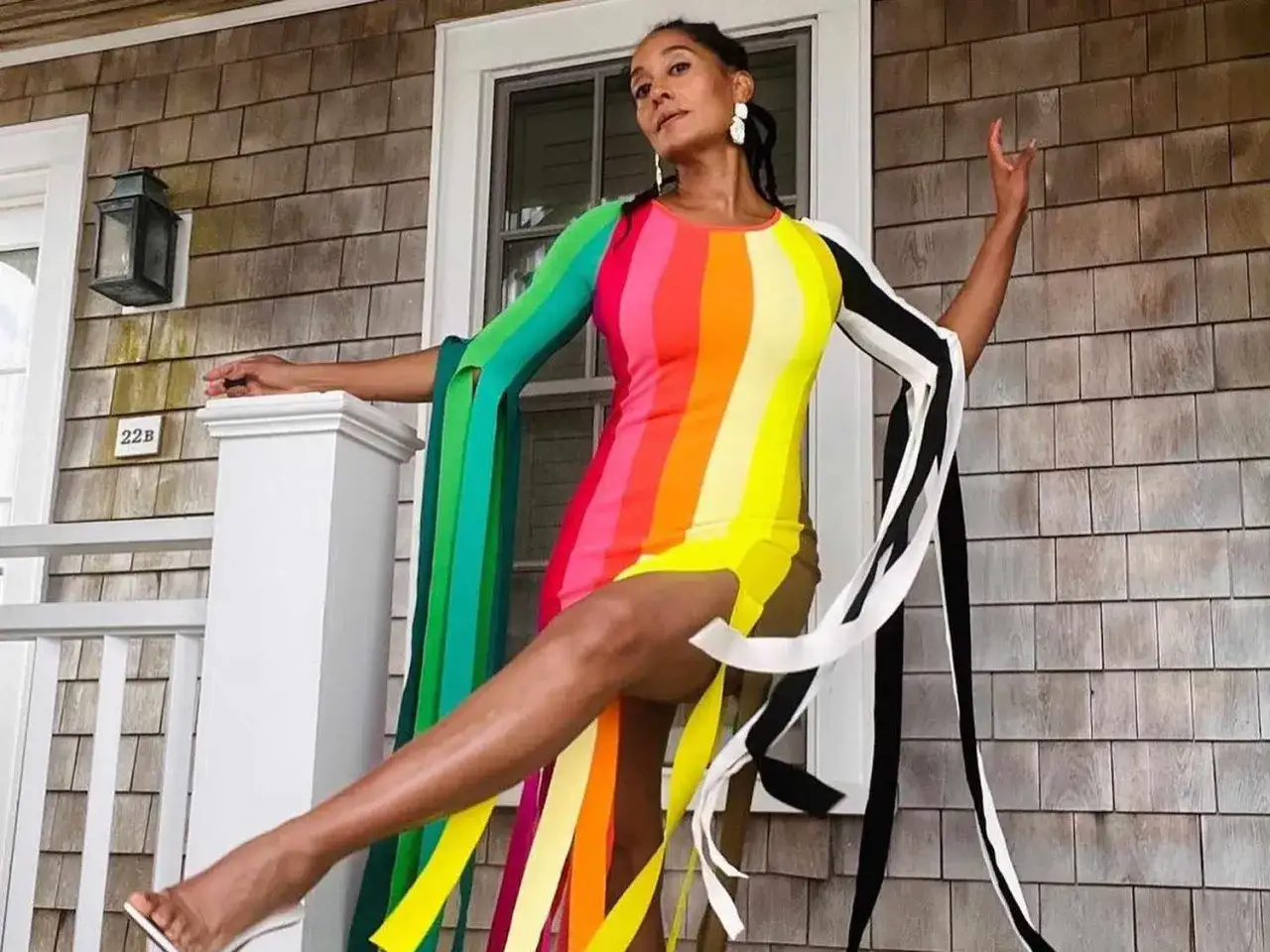 Une femme pose sur un porche, vêtue d'une robe audacieuse en color blocking arc-en-ciel avec des manches originales.