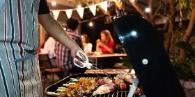 Un homme en tablier rayé prépare un barbecue. Idéal pour savoir comment s'habiller pour un barbecue : décontracté et pratique !