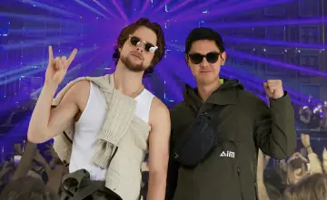 Deux amis profitent d'un concert, l'un fait un signe rock'n'roll, l'autre un poing levé. Leur tenue festival pluie est parfaite pour l'ambiance.