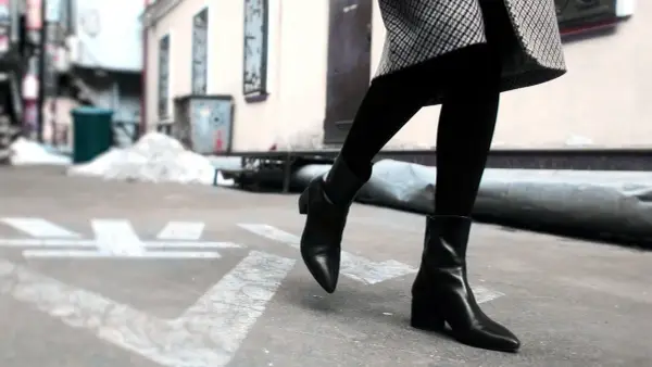 Une femme porte une tenue avec des chelsea boots femme noires, un manteau à carreaux et des collants.