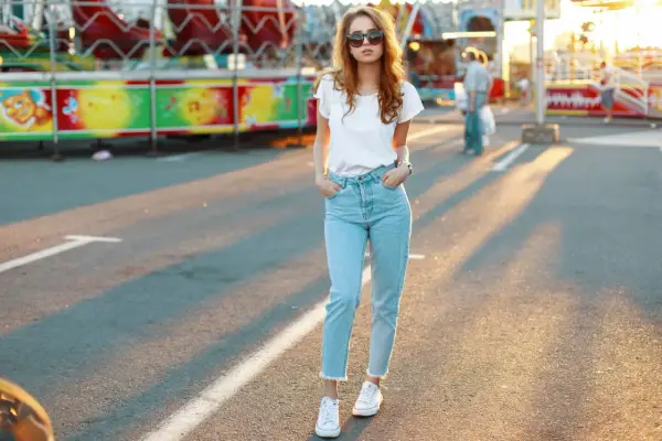 Une jeune femme porte un jean mom et des baskets blanches, un look parfait pour une journée à la fête foraine.