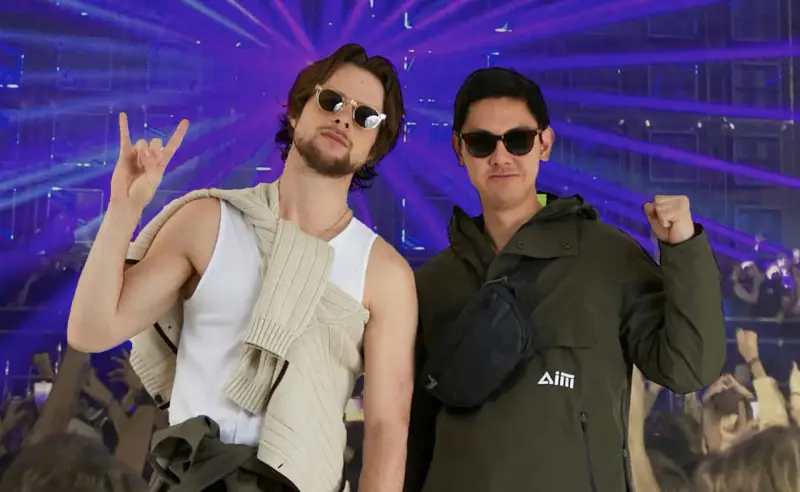 Deux amis profitent d'un concert, l'un fait un signe rock'n'roll, l'autre un poing levé. Leur tenue festival pluie est parfaite pour l'ambiance.