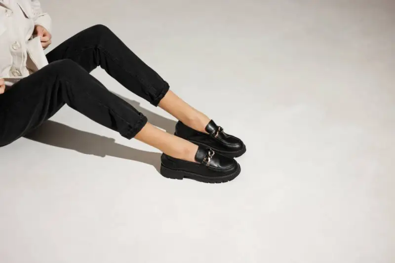 Une tenue décontractée avec un jean noir et une veste claire, rehaussée par une élégante tenue avec mocassin femme orné d'une chaîne dorée.